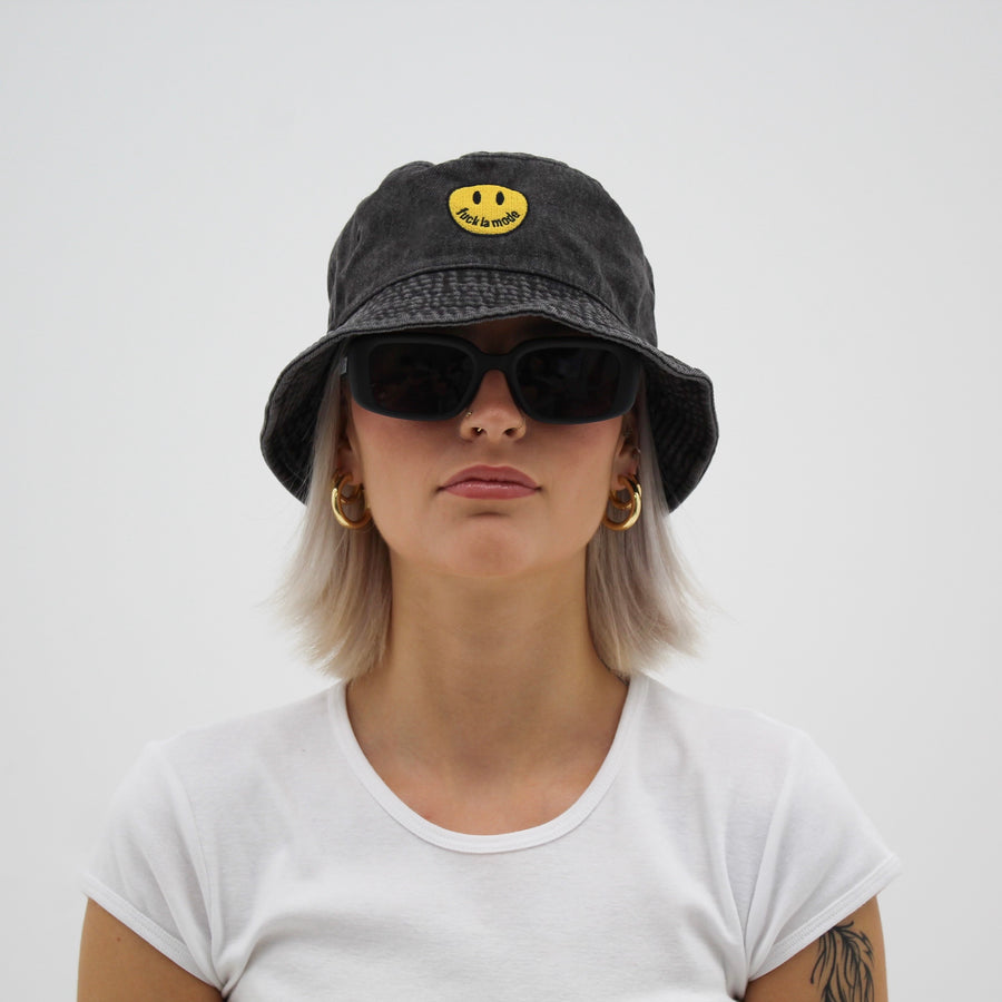 Black denim smiley face bucket hat with a yellow “fuck la mode” smiley face — streetwear clothing from Québec City.