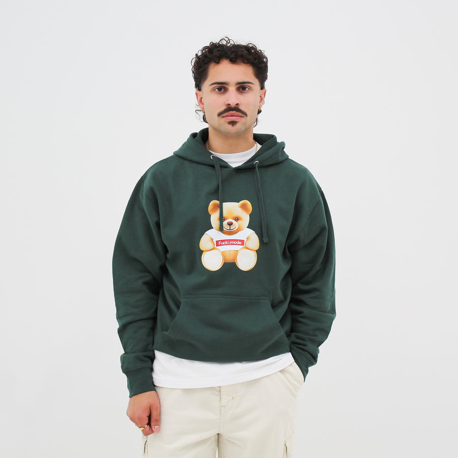 Green “fuck la mode” hoodie with kangaroo pocket, hood drawstring, and the “fuck la mode” teddy bear at the center — streetwear clothing from Québec City.