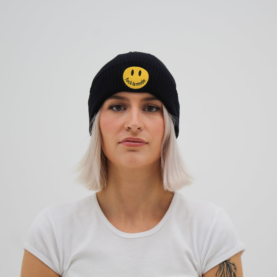 Black “fuck la mode” beanie with yellow “fuck la mode” smiley face — streetwear clothing from Québec City.
