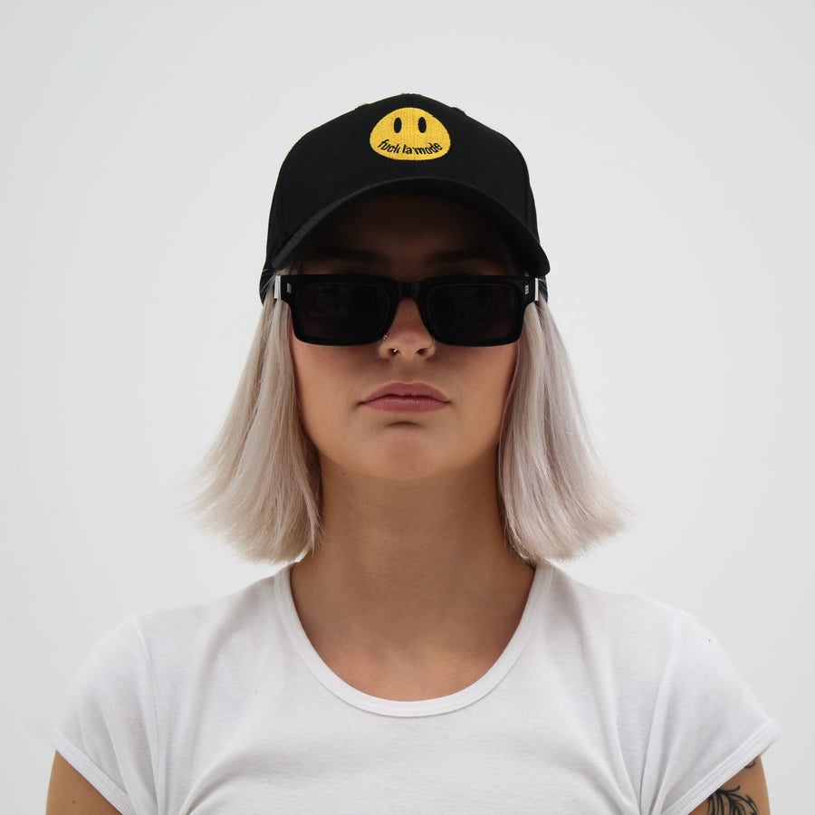 Black trucker hat with a yellow smiley face “fuck la mode” — streetwear clothing from Québec City.