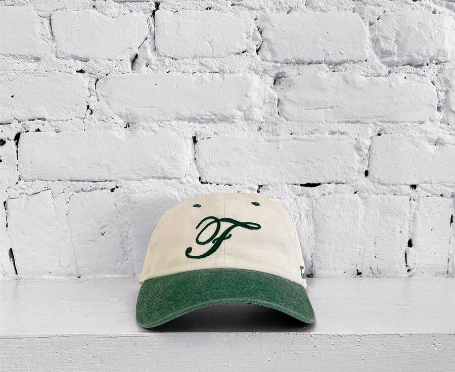 Off-white and green two-tone “F” cap with the “fuck la mode” logo on the side and an “F” on the front — streetwear clothing from Québec City.